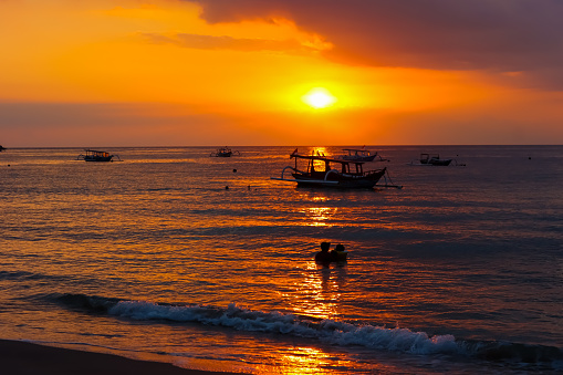 Scenic view of dramatic sunset in the beach with silhouette boats and tourists on the sea