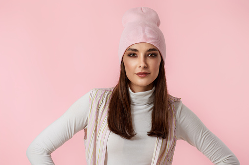 carefree woman in pink hat, shirt looking at the camera on pastel pink background.