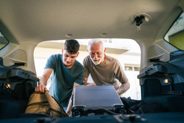 dois homens adolescente e avô idoso embalam bagagem no porta-malas do carro - luggage packing suitcase old - fotografias e filmes do acervo