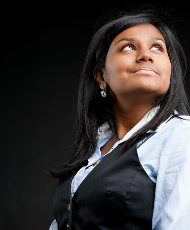 Gazing towards future innovations, a smiling Indian businesswoman in formal attire stands out against a dark gradient background. Copyspace to her left awaits your message