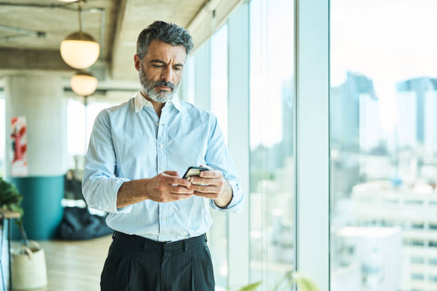 istock Mature businessman using mobile phone standing in office 1691186050
