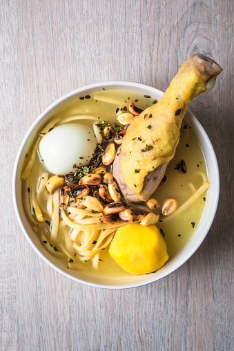 Aerial view of a plate of chicken soup, with hard boiled egg, yellow potato, cancha serrana, noodles and oregano.