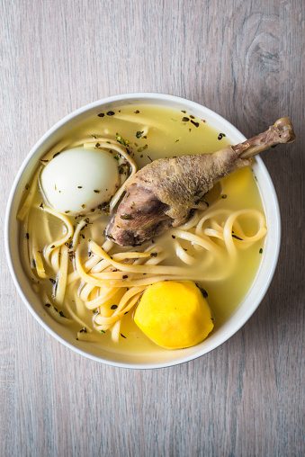 Aerial view of a chicken soup, with hard boiled egg, yellow potato and noodles.