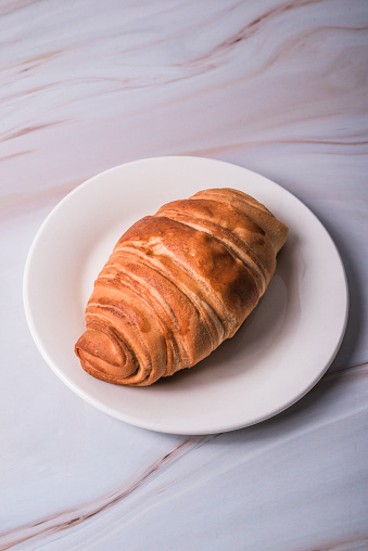 Croissant bread on a plate on a marble table. Food concept.