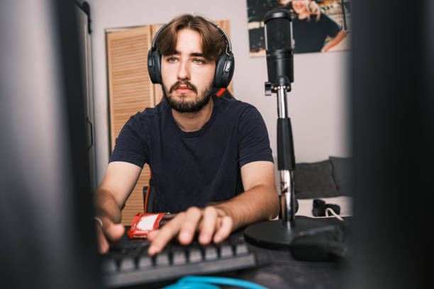 Young Caucasian man streaming with friends online Young Caucasian man eating dark chocolate bar while streaming online, communicating with friends. He is dressed in casual clothes. Interior of youth bedroom during the day. man hand holding candy bar stock pictures, royalty-free photos & images