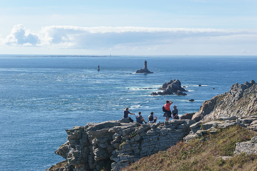 Seascape with people on rocks at the coastline of Pointe du Raz and Vieille lighthouse, Plogoff, Finistere, Brittany, France