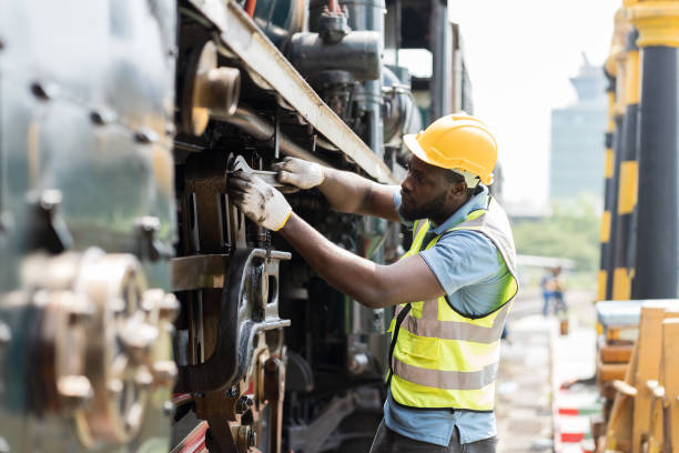 Ingeniero afroamericano de mantenimiento del motor de la locomotora en el taller de reparación de locomotoras. Ingeniero ferroviario masculino usa la rueda del tren de reparación de llaves inglesas en el garaje del tren - foto de stock