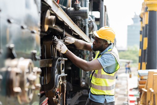 African American male engineer maintenance locomotive engine in locomotive repair garage. Male railway engineer use wrench repair train wheel in train garage