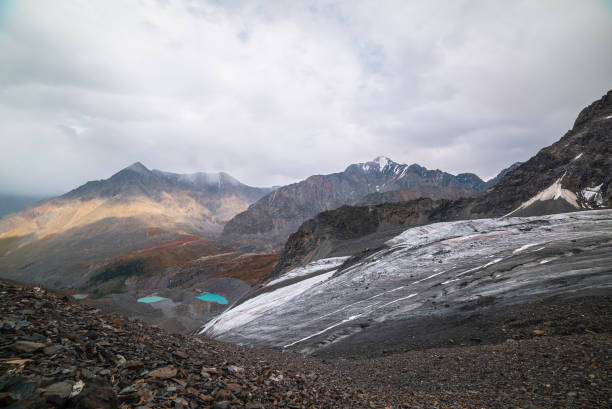 istock Awesome top view from glacier to small turquoise lakes and pyramid shaped mountain. Beautiful lakes among fading autumn colors and high mountain range. Sharp peak in sunlight and shadows of clouds. 1691408112