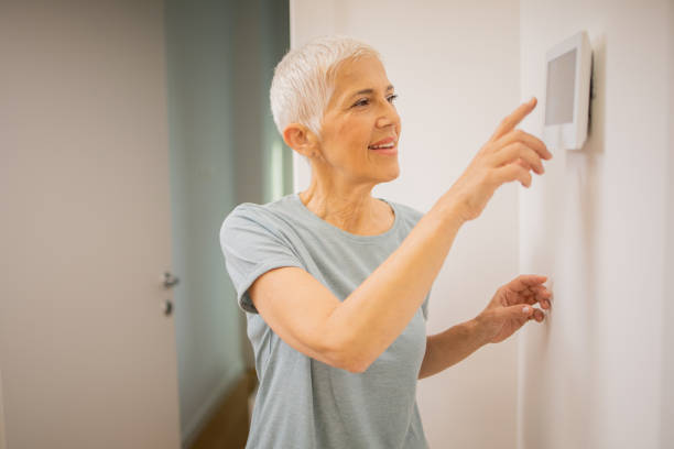 istock Young woman adjusts the temperature at home with a device on the wall 1691409244