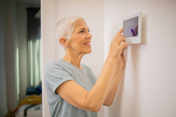istock Young woman adjusts the temperature at home with a device on the wall 1691409253