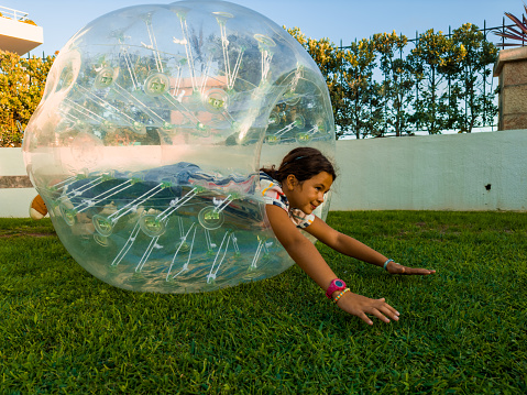 Happy and fun a young girl in her garden plays with a transparent ball