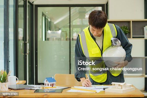 A male engineer asian working on a blueprint architectural project at a construction site at a desk in the office.