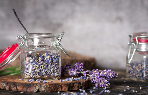 Lavender flowers placed in two glass jars on a wooden table and gray background. Ready to use as tea or aromatherapy. The scent of serenity and tenderness