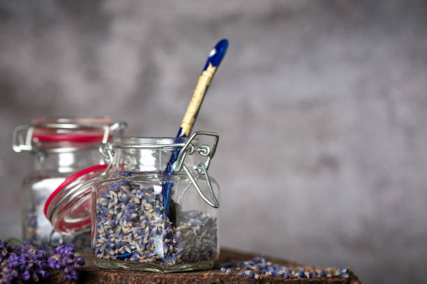 Lavender flowers placed in two glass jars on a wooden table and gray background. Ready to use as tea or aromatherapy. The scent of serenity and tenderness