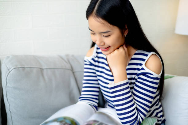 istock Asian woman reading a book while relaxing and sitting on the sofa 1691468486