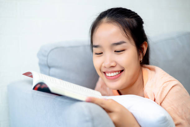 istock Asian woman reading a book while relaxing and lying on the sofa 1691471132