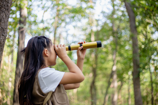 Happy Little Asian girls looking ahead and smiling child with the binoculars in the park. Travel and adventure concept. Freedom, vacation