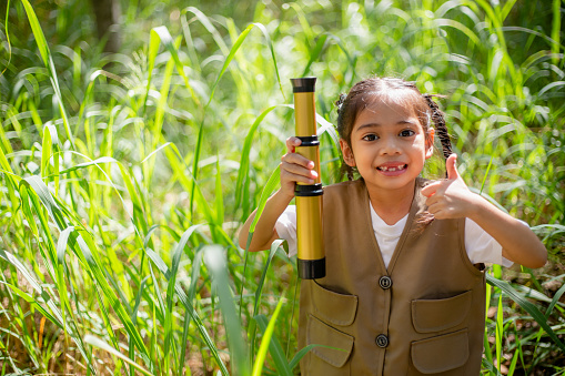 Asian little girls explore nature through magnifying glasses and binoculars in the park. Education, field trips, research, and discovery concepts.