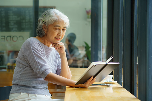 An Asian senior woman reading a book in a cafe.