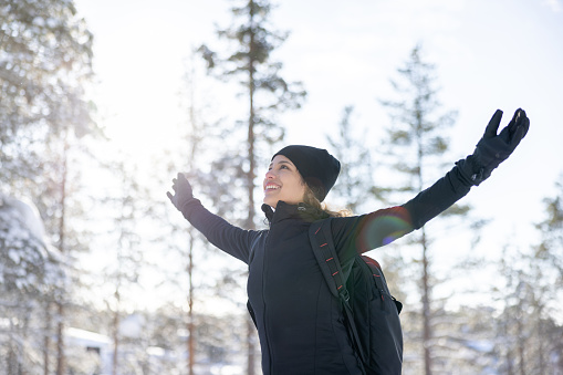 Happy woman hiking in the winter and enjoying the snow while looking up with arms open