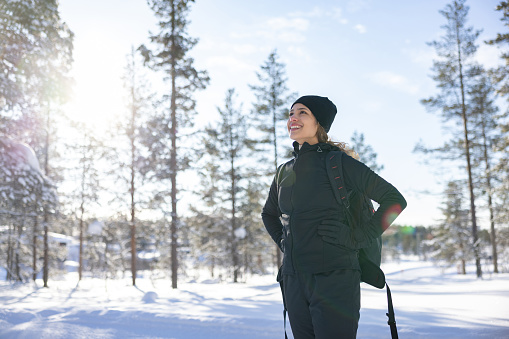 Happy woman hiking in the winter and looking at the landscape while carrying her backpack
