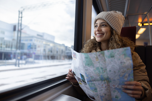 Portrait of a happy tourist traveling by train and holding a map and looking through the window