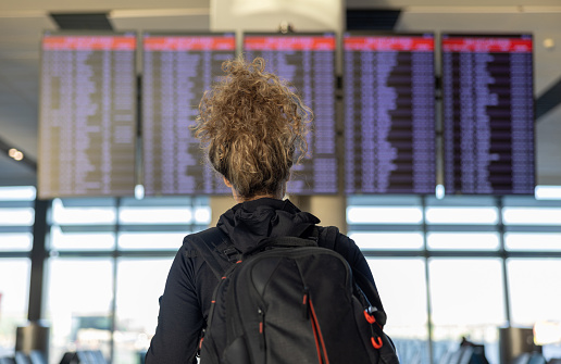 Rear view of a female traveler at the airport looking at the arrival departure board - travel concepts