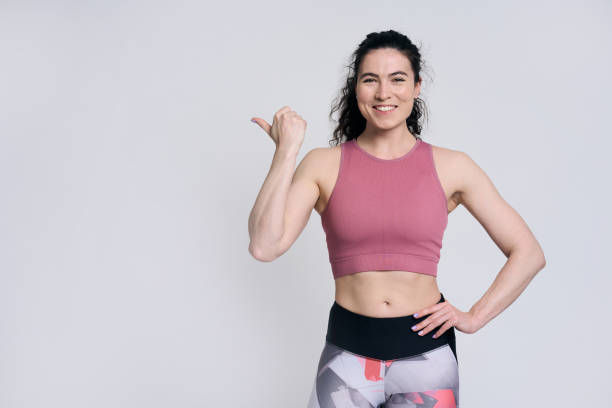 istock Beautiful female athlete smiling looking at camera, pointing aside at copy space on white background 1691541968