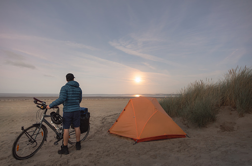 man with touring bike camping on beach under full moon in Wales, England, United Kingdom