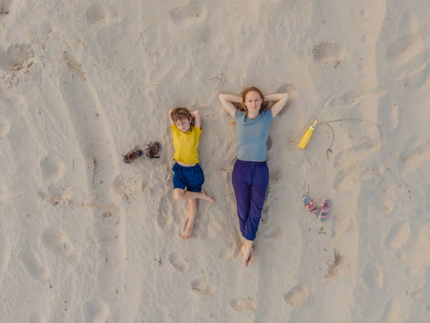 Mom and son are lying on the sand at sunset. View from the drone. Paradise, travel, vacation concept Mom and son are lying on the sand at sunset. View from the drone. Paradise, travel, vacation concept. girls laying on beach stock pictures, royalty-free photos & images