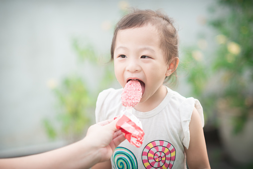 Captured in a moment of pure delight, a 3-year-old Chinese baby girl savors the sweetness of her ice cream cone with unbridled joy. Her eyes sparkle with happiness as she takes her first delicious bite, a heartwarming scene that radiates innocence and happiness.