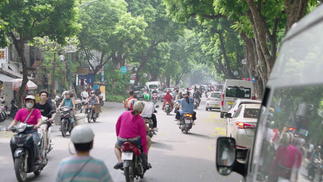 people on mopeds and scooters travelling on a busy street in Vietnam. The people are backlit from the setting sun.