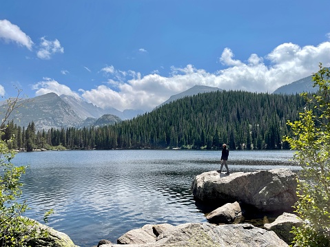 Active senior man in distance stands on large boulder at Bear Lake in the Rocky Mountains of Colorado against lake, mountains,  blue sky and clouds
