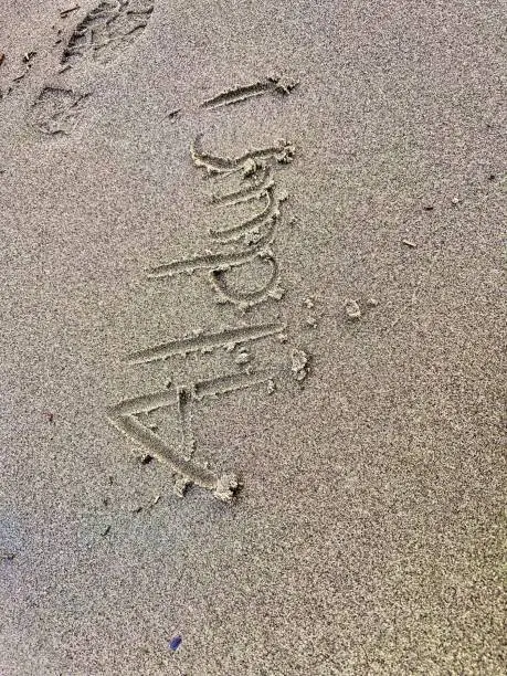 Photo of Close-up of the word 'Alduri' drawn in the sand on a beach