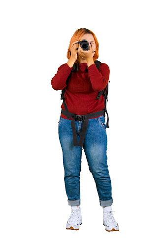 Young female photographer in casual winter clothes looking at viewfinder taking photos isolated over white background