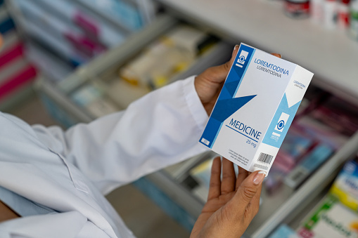 Close-up on a pharmacist holding a box of prescription medicine at the drugstore - healthcare and medicine concepts