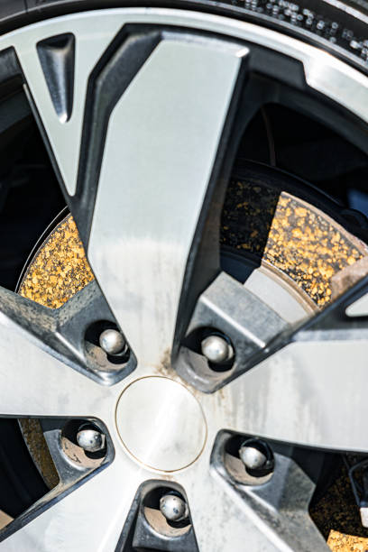 Close-up view through gaps in the aluminum alloy wheel of a modern car looking at the rusted disc brake rotor. It's a sunny day after a few days of heavy rain while the car was parked. This rusting is very common, and doesn't cause driving problems. When the vehicle is again driven, the disc brake calipers and brake pads engage during braking. As soon as the pads squeeze against the rotor to slow the car down, most of the rust on the rotors is automatically removed.