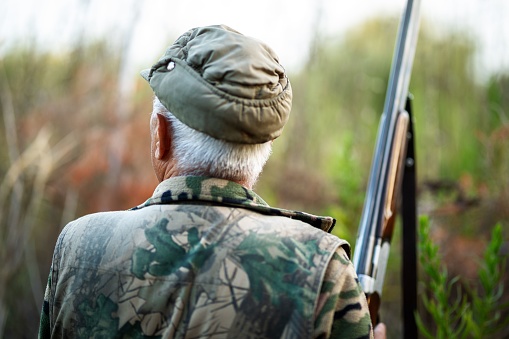 A rear view of a mature male with a camouflage outfit and a gun in a forest