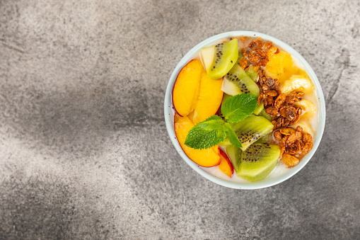 Granola bowl with yogurt and fresh almonds, blueberries, raspberries,peach, kiwi, strawberries and banana on textured kitchen table.Acai and spirulina bowl.Healthy breakfast concept. Copy space.