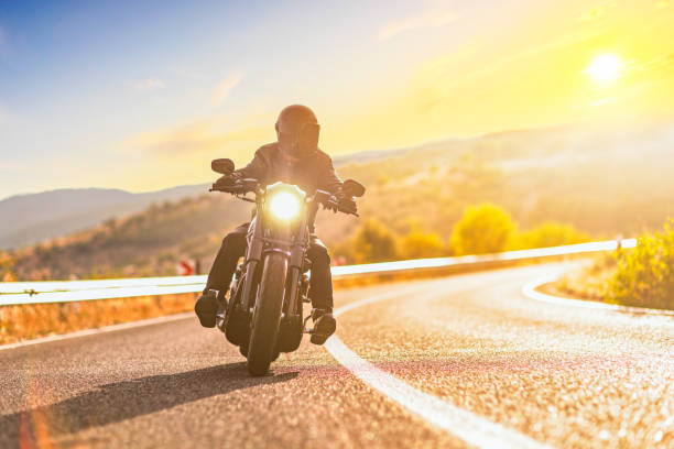 puesta de sol sobre una carretera abierta y un hombre con casco montando una moto - motociclista fotografías e imágenes de stock