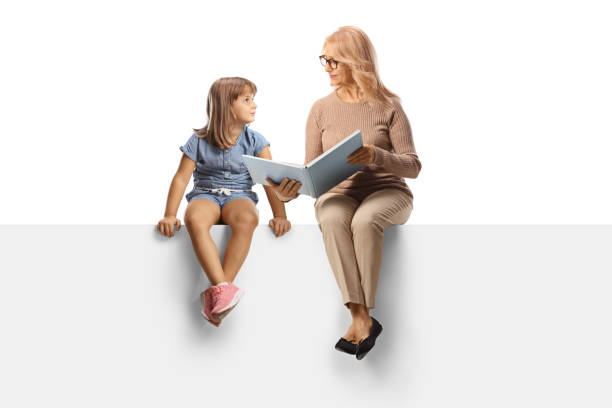 woman reading a book to a little girl and sitting on a blank panel - child women outdoors mother imagens e fotografias de stock