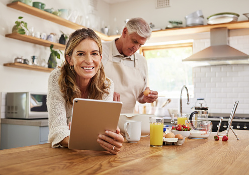 Tablet, baking and retirement with a senior couple cooking in the kitchen of their home together. Food, technology and health with an elderly man and woman following an internet recipe to make a meal