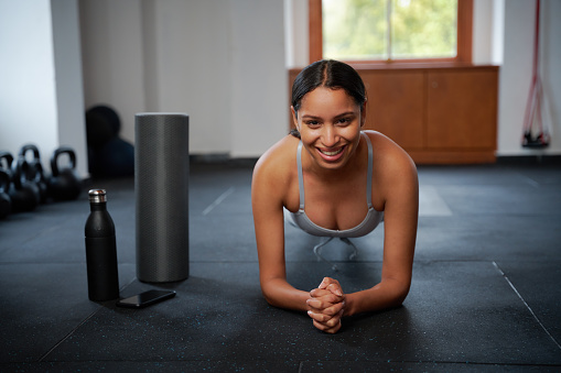 Confident young biracial woman in sportswear doing plank exercises at the gym