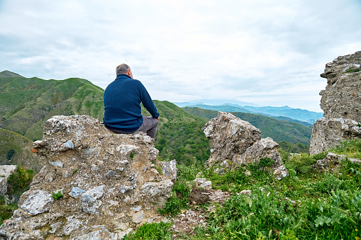 Mature traveler man enjoying freedom on the pick of mountain in front of panoramic view of serene fall nature. Mental health, wellbeing, trip adventure and healthy lifestyle.