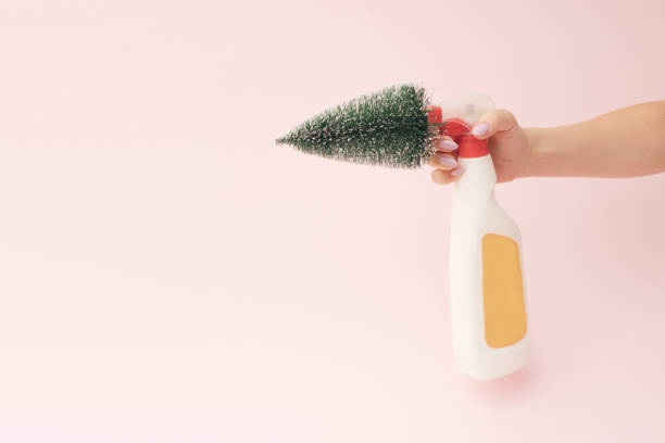 A beautiful female hand holds a cleaning agent with a Christmas tree. Pink background.