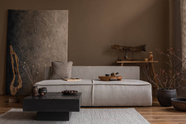 istock Creative composition of wabi sabi living room interior with mock up poster frame, modular sofa, stylish coffee table, vase with branch, wooden decoration and personal accessories. Home decor. Template 1691851682