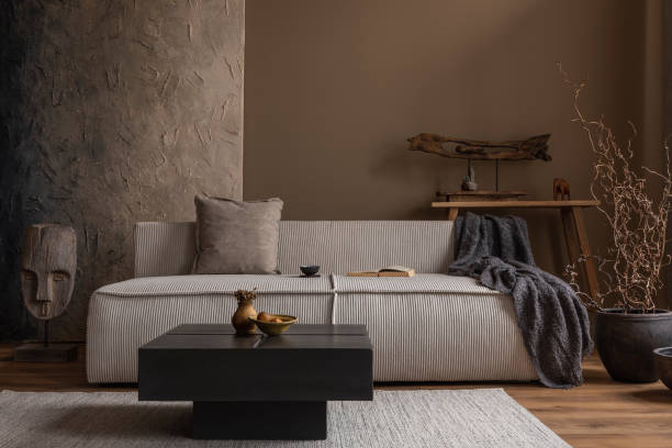 istock Creative composition of wabi sabi living room interior with mock up poster frame, modular sofa, stylish coffee table, vase with branch, wooden decoration and personal accessories. Home decor. Template 1691851695