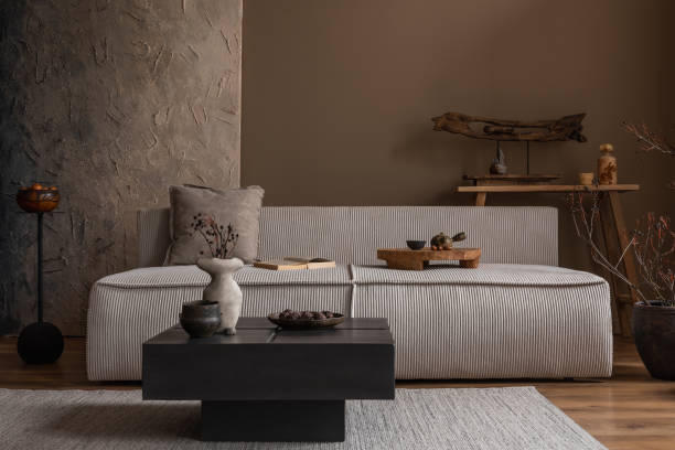 Creative composition of wabi sabi living room interior with mock up poster frame, modular sofa, stylish coffee table, vase with branch, wooden decoration and personal accessories. Home decor. Template.