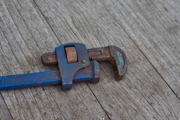 Rusty blue pipe wrench with open jaws on wooden table.